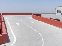 an asphalt parking lot with concrete walls and red and white accents and walls, a green fenced area, and an air field on the far side