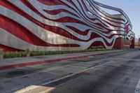 a man walks down the street past a big red and white wave building with a large silver wave building on one side