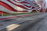 a man walks down the street past a big red and white wave building with a large silver wave building on one side