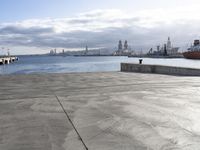 the skateboarder was riding across an empty dock with ships in the background,