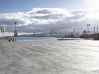 the skateboarder was riding across an empty dock with ships in the background,