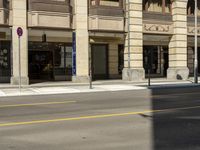 a car is driving down the street past some shops in a building complex where there are people and two street signs on both sides