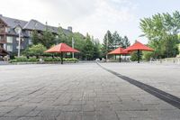 several empty benches and umbrellas on a brick street with trees in the background in the city park