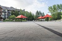 several empty benches and umbrellas on a brick street with trees in the background in the city park