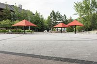 several empty benches and umbrellas on a brick street with trees in the background in the city park