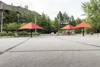 several empty benches and umbrellas on a brick street with trees in the background in the city park