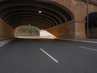 a long road passes underneath an overpass with arches and lights overhead, below is an empty street