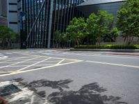 a paved road with many yellow stripes near a tall glass building and trees in the city