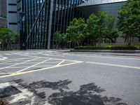 a paved road with many yellow stripes near a tall glass building and trees in the city