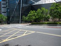 a paved road with many yellow stripes near a tall glass building and trees in the city