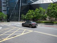 a paved road with many yellow stripes near a tall glass building and trees in the city