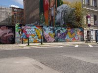 a city side view of a mural on the side of a building with a wall of many colorful paintings, some have different faces