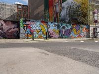 a city side view of a mural on the side of a building with a wall of many colorful paintings, some have different faces