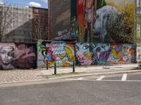 a city side view of a mural on the side of a building with a wall of many colorful paintings, some have different faces