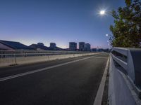 a view of city skyline from across a bridge at twilight time, with two street lights over it