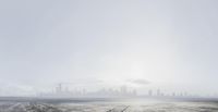 the city is visible from behind an empty air field with footprints on the ground and fog