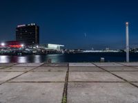 a large, square cement walkway next to a body of water with a fire hydrant and a city skyline in the distance