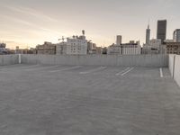 a large empty parking lot is on a concrete lot with city buildings in the background