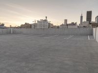 a large empty parking lot is on a concrete lot with city buildings in the background