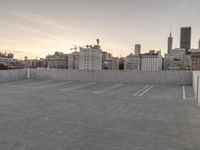 a large empty parking lot is on a concrete lot with city buildings in the background