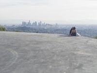 people sitting on a rock overlooking a city skyline and a hill with a skateboard