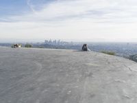 people sitting on a rock overlooking a city skyline and a hill with a skateboard