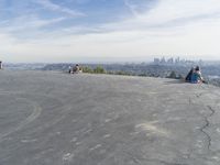 people sitting on a rock overlooking a city skyline and a hill with a skateboard