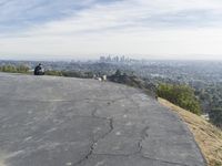 people sitting on a rock overlooking a city skyline and a hill with a skateboard