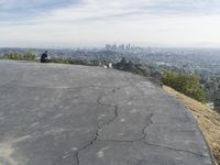 people sitting on a rock overlooking a city skyline and a hill with a skateboard