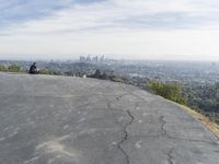 people sitting on a rock overlooking a city skyline and a hill with a skateboard