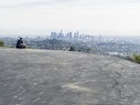 people sitting on a rock overlooking a city skyline and a hill with a skateboard