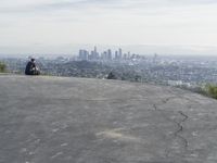 people sitting on a rock overlooking a city skyline and a hill with a skateboard