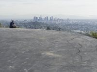 people sitting on a rock overlooking a city skyline and a hill with a skateboard