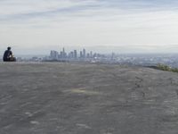 people sitting on a rock overlooking a city skyline and a hill with a skateboard