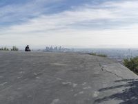 people sitting on a rock overlooking a city skyline and a hill with a skateboard