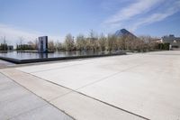 concrete walkway and fountain in front of large, blue glass structure that looks like a mountain