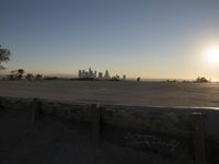 the sun sets over the city skyline in a beachfront area of a fenced off parking lot