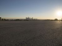 the sun sets over the city skyline in a beachfront area of a fenced off parking lot