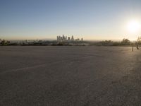 the sun sets over the city skyline in a beachfront area of a fenced off parking lot