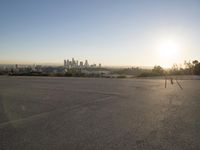 the sun sets over the city skyline in a beachfront area of a fenced off parking lot