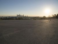 the sun sets over the city skyline in a beachfront area of a fenced off parking lot