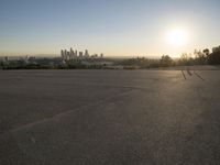 the sun sets over the city skyline in a beachfront area of a fenced off parking lot