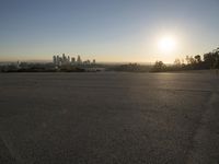 the sun sets over the city skyline in a beachfront area of a fenced off parking lot