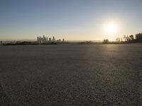 the sun sets over the city skyline in a beachfront area of a fenced off parking lot