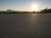 the sun sets over the city skyline in a beachfront area of a fenced off parking lot