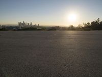 the sun sets over the city skyline in a beachfront area of a fenced off parking lot