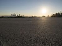 the sun sets over the city skyline in a beachfront area of a fenced off parking lot