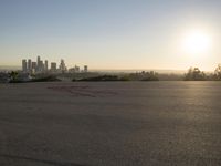 the sun sets over the city skyline in a beachfront area of a fenced off parking lot