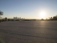 the sun sets over the city skyline in a beachfront area of a fenced off parking lot