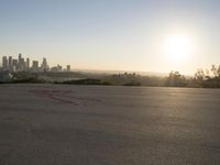 the sun sets over the city skyline in a beachfront area of a fenced off parking lot